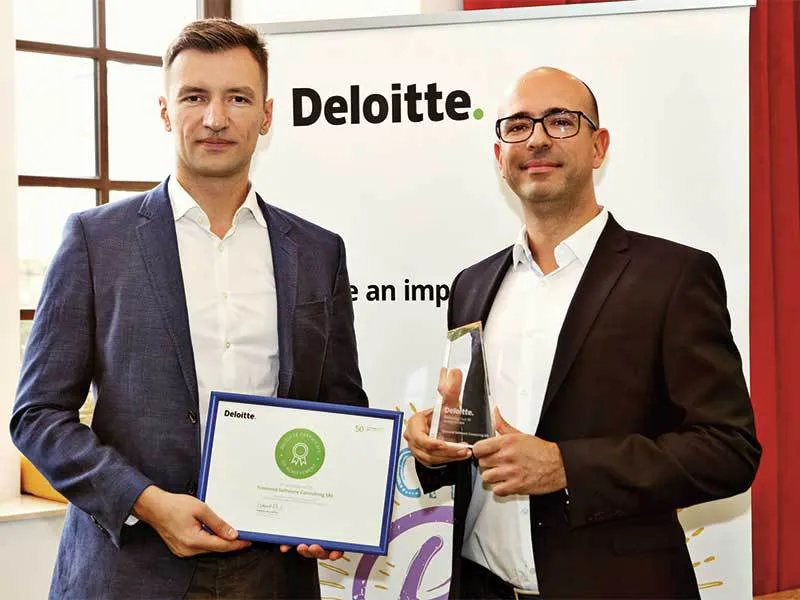 Marius Hanganu (stânga), cu o diplomă Deloitte înrămată, și Ioan Cocan, cu un trofeu de sticlă, în sacouri închise, în fața unui banner Deloitte.