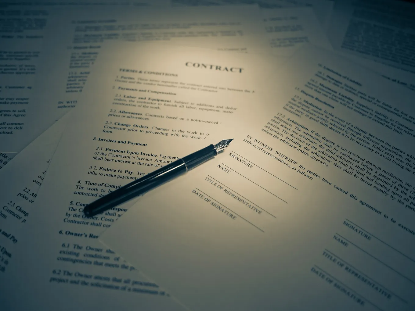 Un stilou așezat pe un contract tipărit, deschis la rubricile pentru semnătură, cu alte pagini împrăștiate în jur.