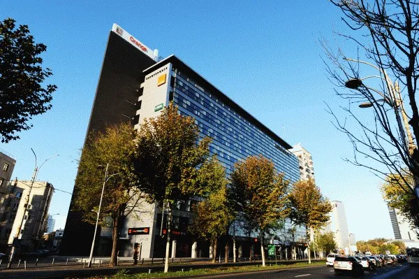 Clădirea de birouri Europe House de pe Bulevardul Lascăr Catargiu din București, cu fațada înaltă de sticlă în spatele copacilor tomnatici, sub cer senin.