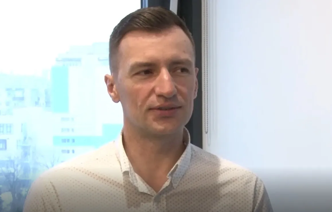 Marius Hanganu, în cămașă deschisă la culoare cu model mărunt, vorbind într-un interviu, lângă o fereastră cu vedere spre clădiri.