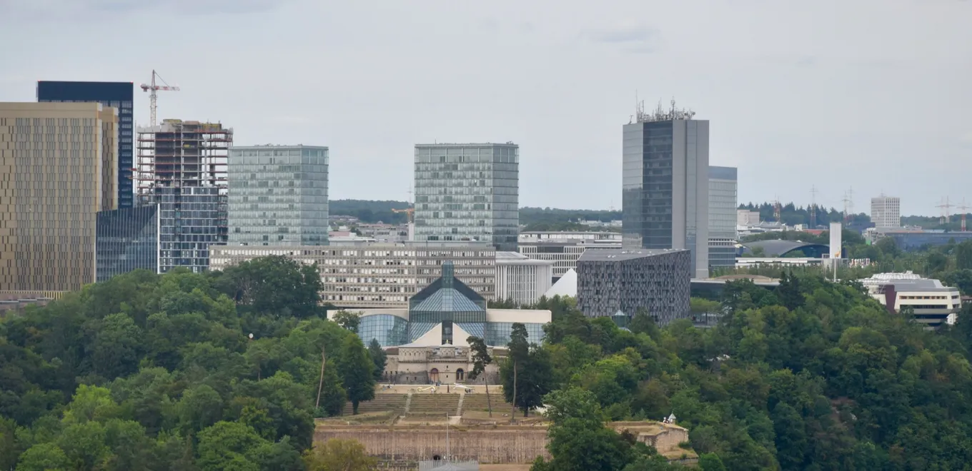 Cartierul european Kirchberg din orașul Luxemburg, cu turnurile de birouri în spatele muzeului Mudam și al Fortului Thüngen, deasupra pantelor împădurite.