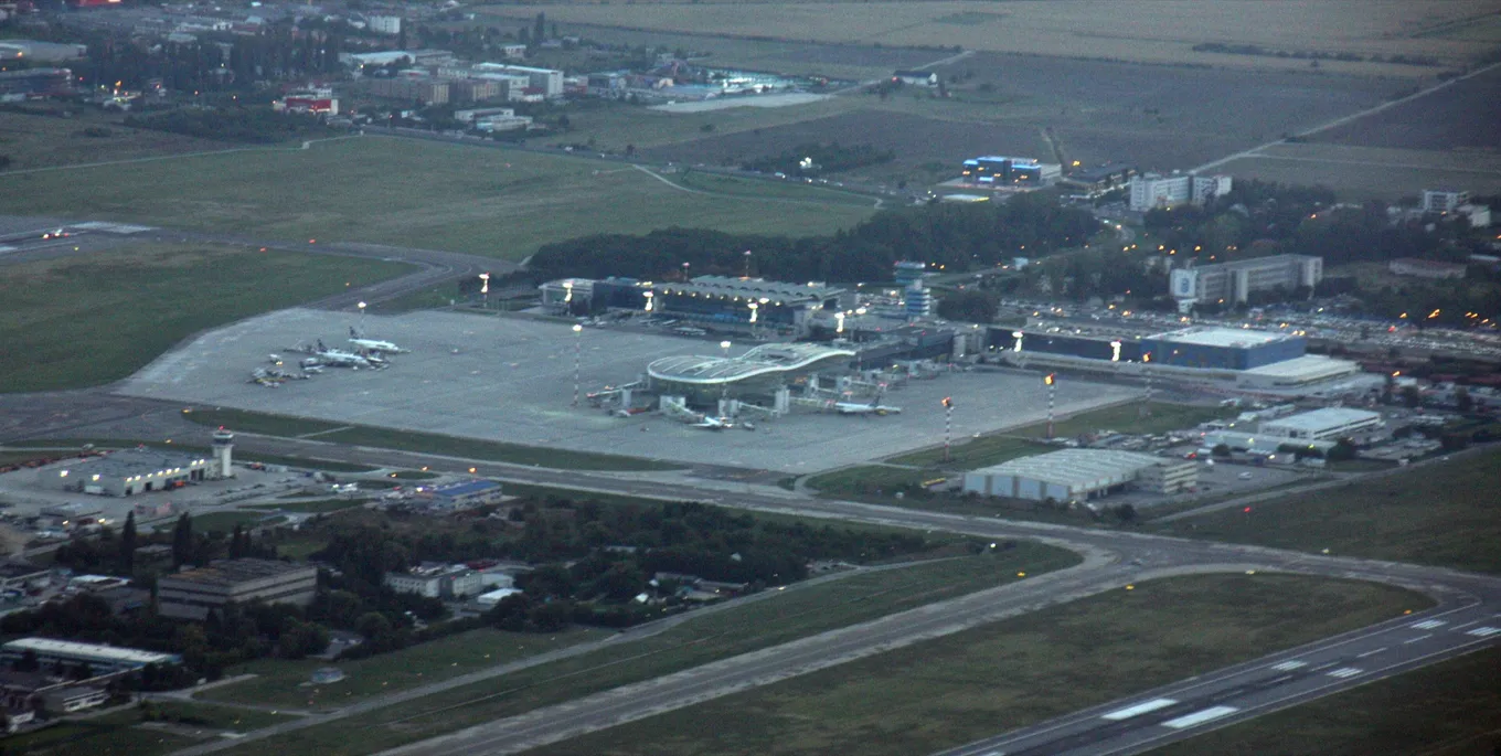 Vedere aeriană la apus a Aeroportului Internațional Henri Coandă de lângă București, cu terminalul, avioane parcate și pista.