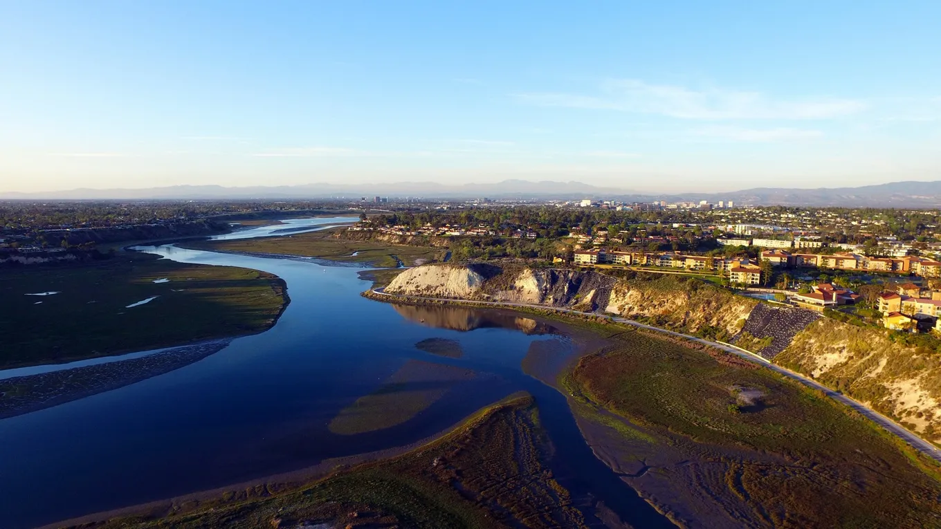 Vedere aeriană asupra golfului Back Bay din Newport Beach, Orange County, California: un braț de apă șerpuit, maluri abrupte în soare și orașul întins până la dealuri.
