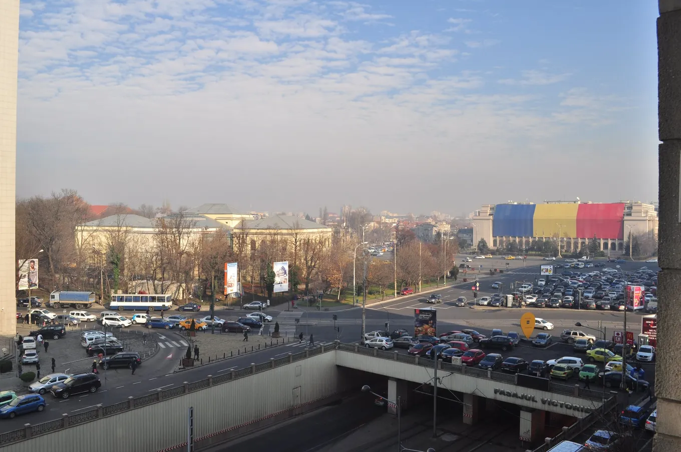 Piața Victoriei din București văzută de sus, cu Palatul Victoria, sediul Guvernului României, acoperit cu un steag uriaș al României, în dreapta.