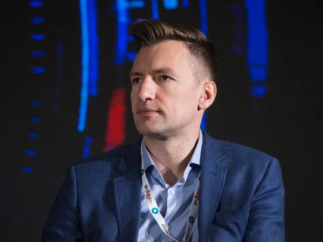 Marius Hanganu pe scena ZF Digital Summit 2018, în sacou albastru și cu ecuson la gât, privind în lateral, pe fundalul unui ecran întunecat.