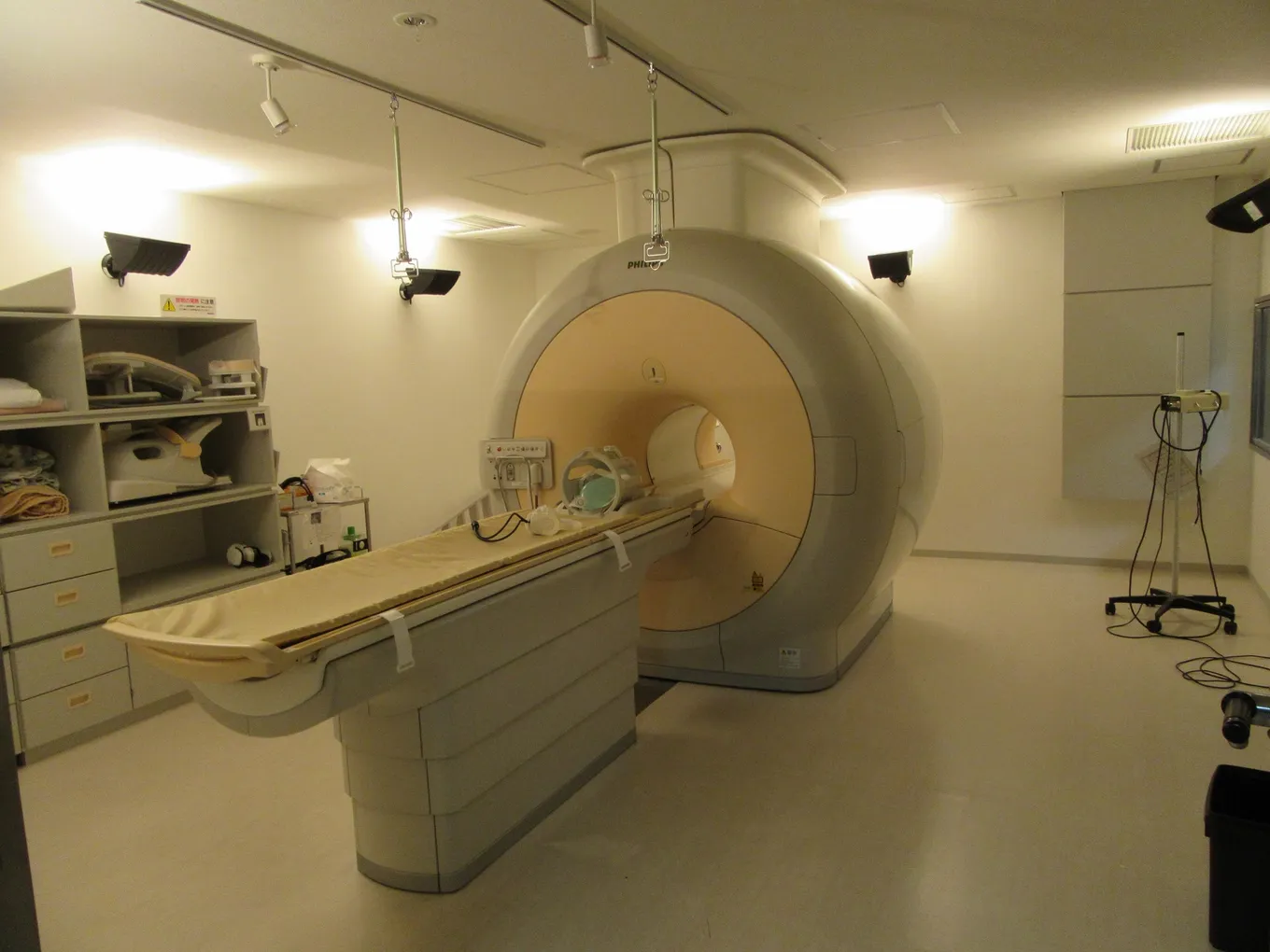 O cameră de spital goală cu un aparat RMN, masa pentru pacient și o bobină pentru cap pregătită pentru următoarea investigație.